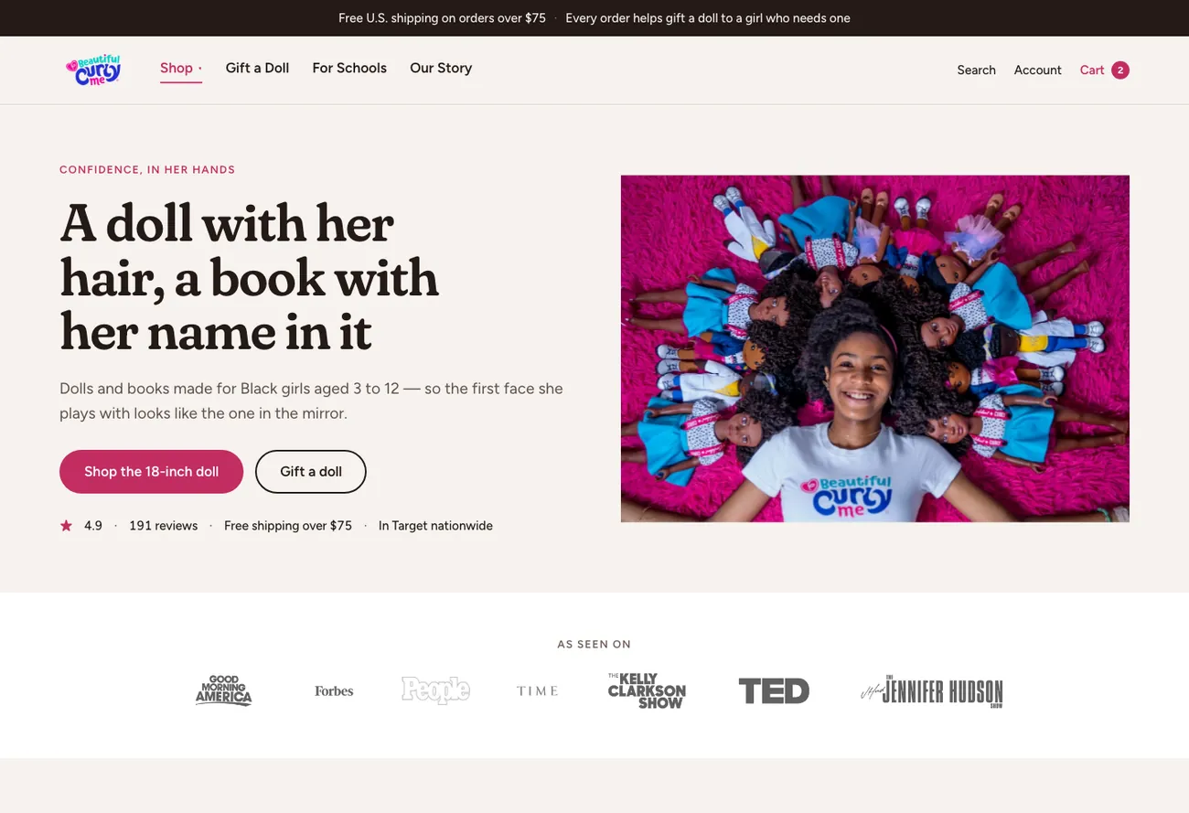 Homepage direction B: the headline "A doll with her hair, a book with her name in it" beside a photograph of Zoe Oli lying on a pink rug ringed by her dolls, above a press logo strip